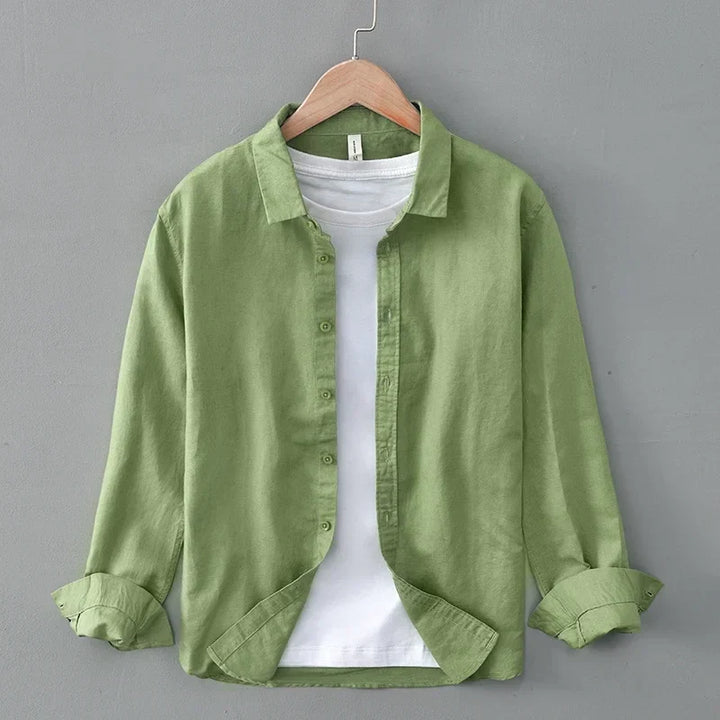 Green linen shirt with rolled sleeves on hanger, against gray wall.
