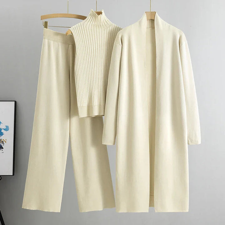Cream-colored three-piece set with sleeveless ribbed top, wide-leg pants, and long open cardigan on hangers in a studio setting.