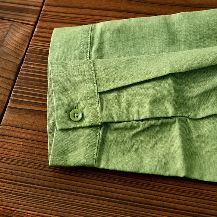Green linen shirt sleeve with button detail on wooden surface.