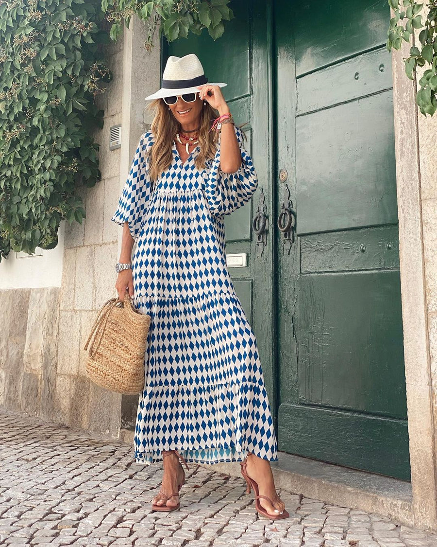 Person in blue and white checkered bohemian long dress, straw hat, and sunglasses, standing by a green door.