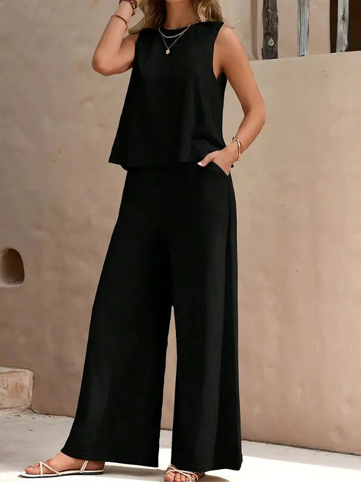 Black sleeveless two-piece set with wide-leg pants, styled outdoors against a beige wall.