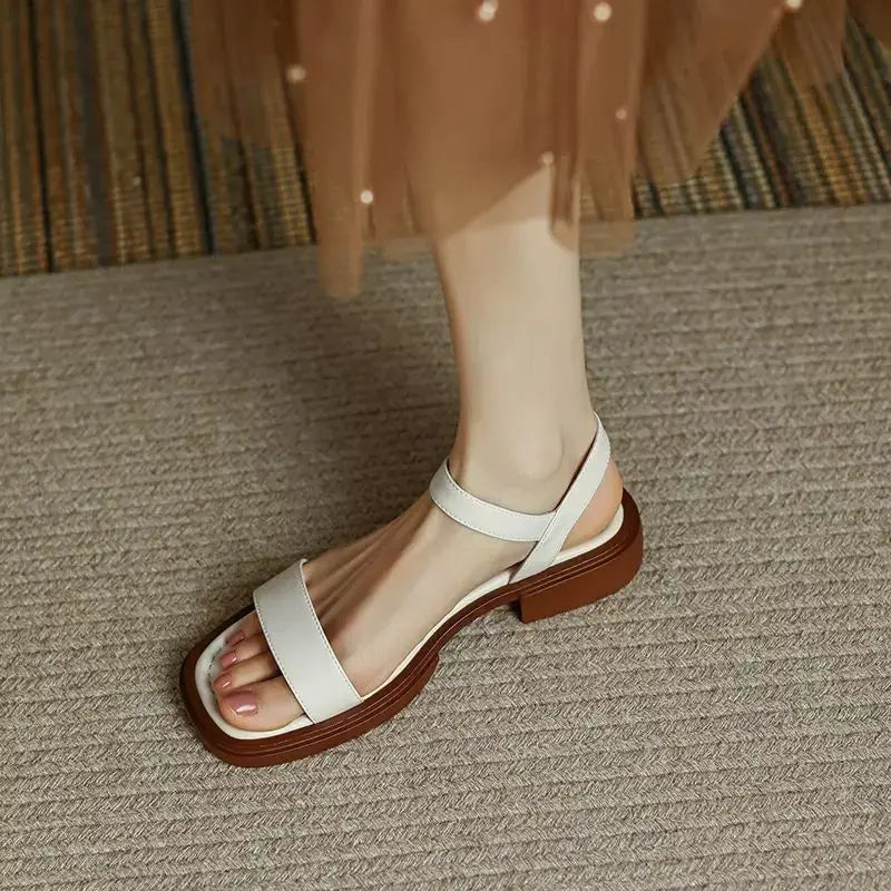 White sandals on foot, textured surface, wearing brown dress.