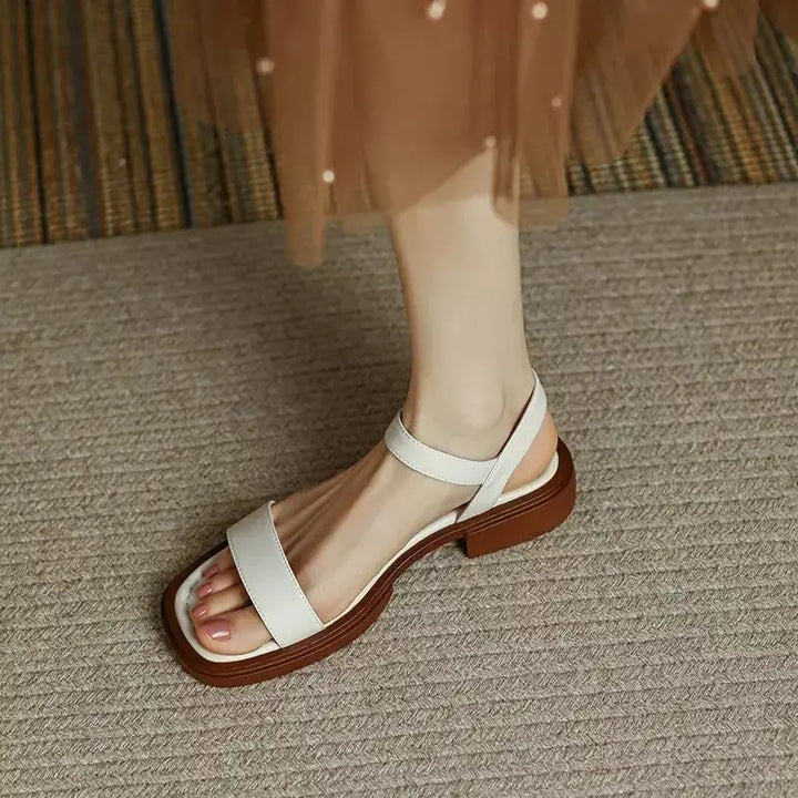 White sandals on foot, textured surface, wearing brown dress.