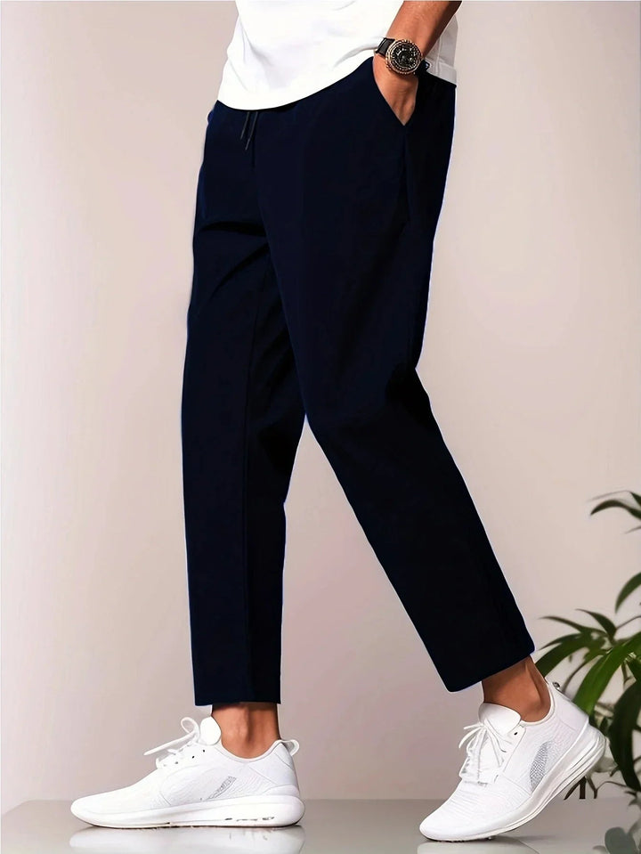 Smart navy trousers matched with a white tee and white sneakers, in a studio environment.