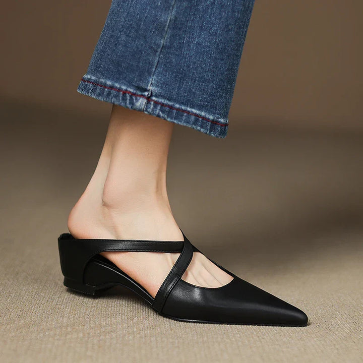 Side view of black mules with criss-cross straps worn with jeans.
