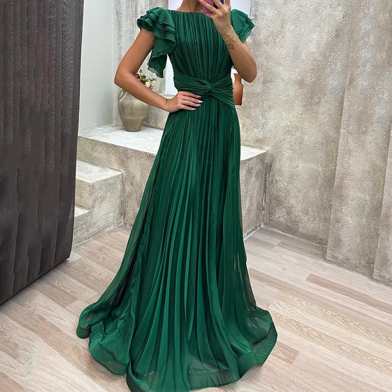Elegant green pleated evening dress with ruffled sleeves, modeled in a chic indoor setting with modern decor.