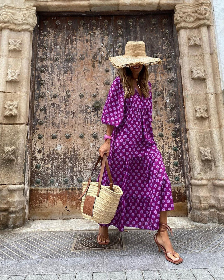 Purple patterned bohemian long dress and straw hat in front of ornate wooden doors outdoors.