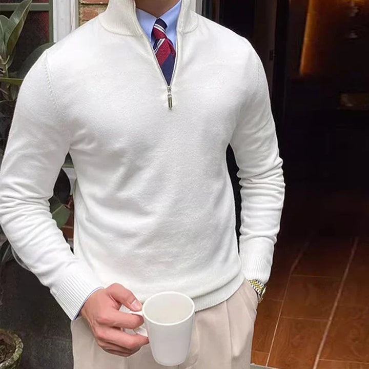 White half-zip sweater with shirt and tie, holding a mug, against a brick and plant background.