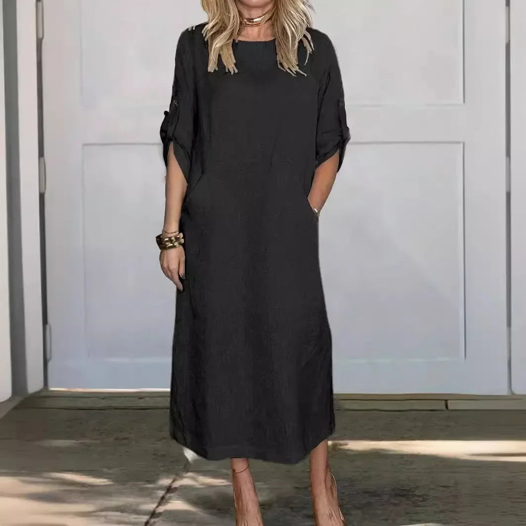 Black A-line loose fit draped evening dress, studio setting with wooden floor and pale wall background.