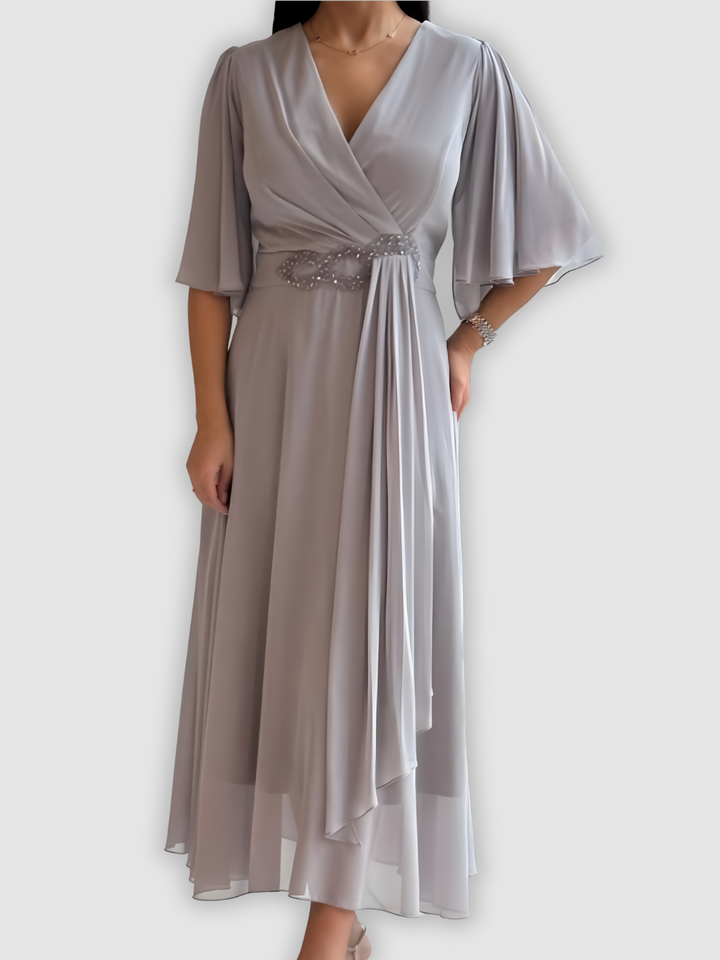Elegant light gray maxi dress with draped design and embellished waistband in a soft studio setting.
