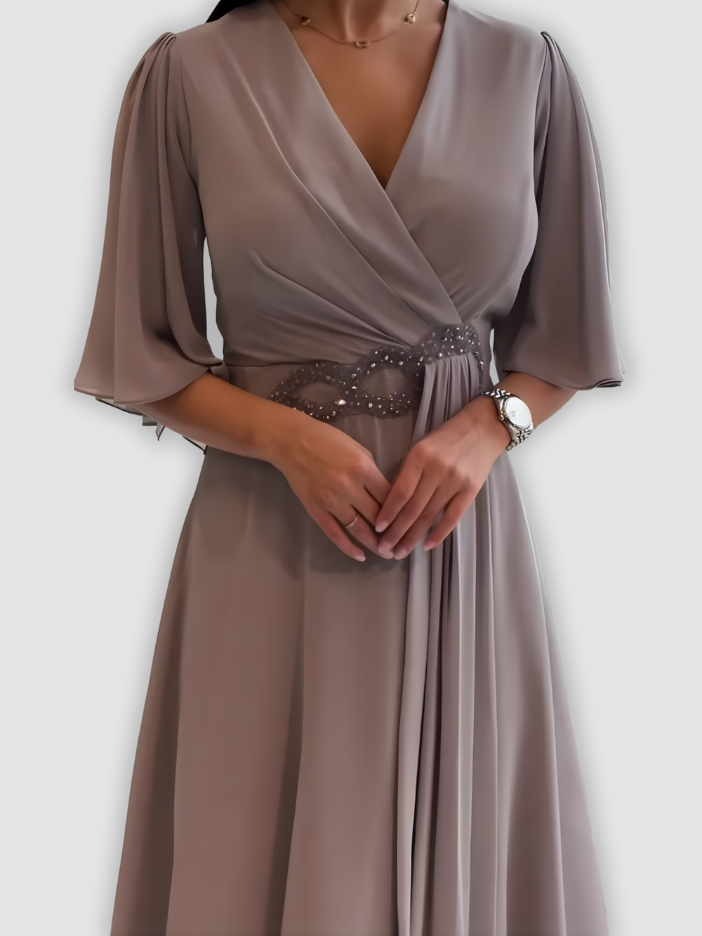 Close-up of light gray maxi dress with detailed embellishments and flowing sleeves in a studio background.