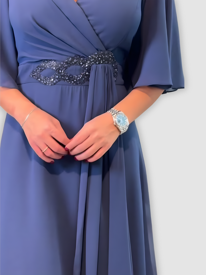 Close-up of dark blue maxi dress with intricate beadwork at the waist in a soft, elegant studio background.