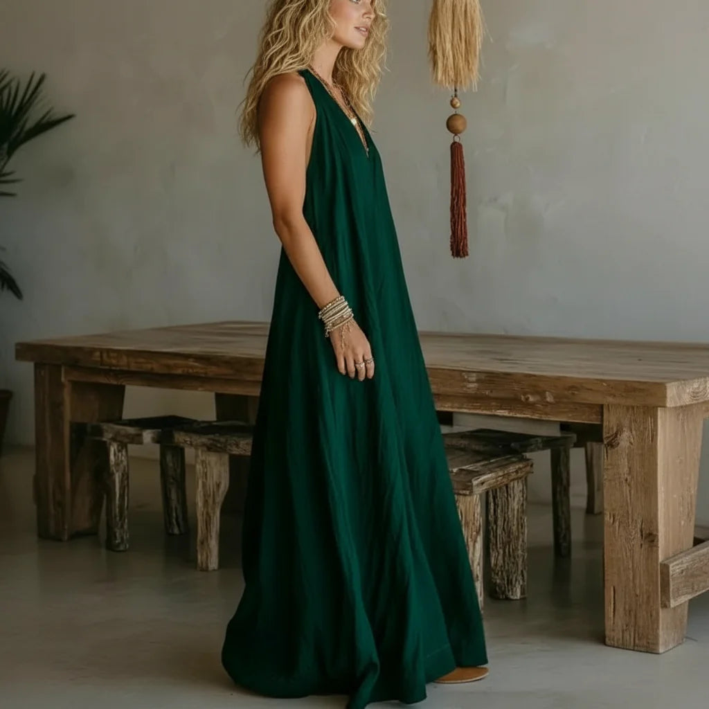 Woman in a green maxi dress standing in a rustic room with wooden furniture and minimalistic decor.