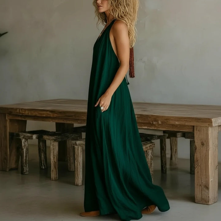 Side profile of a woman in a green maxi dress standing in a rustic room with wooden furniture and decor.