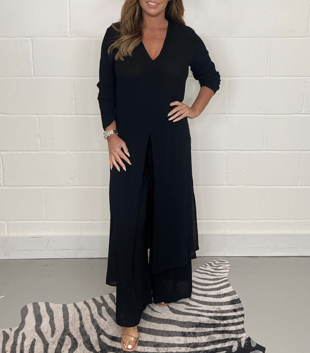 Black two-piece set with long sleeves, V-neck, and flowing pants in a studio with zebra rug.