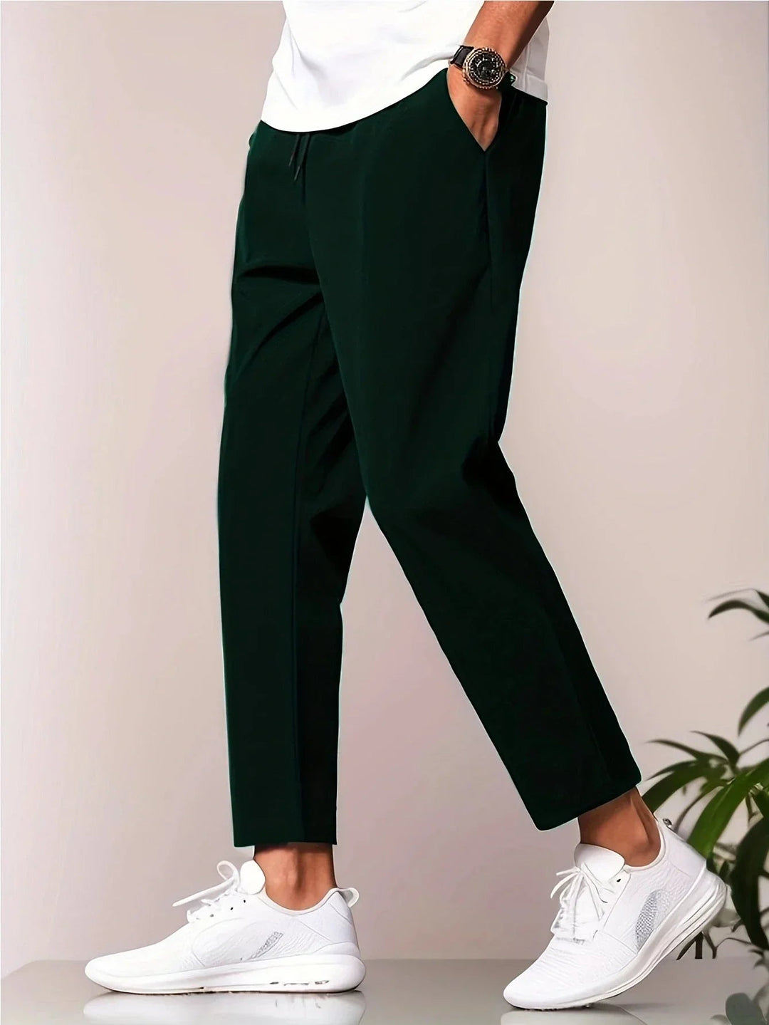 Elegant dark green trousers with a white shirt, styled with white sneakers, studio background.