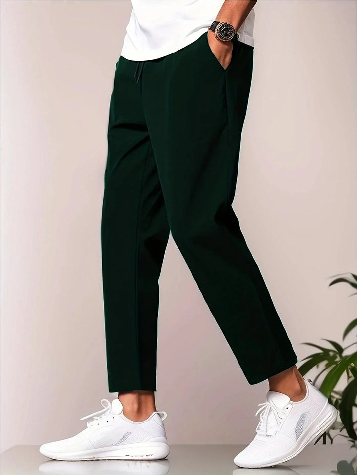 Elegant dark green trousers with a white shirt, styled with white sneakers, studio background.