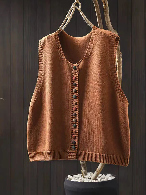 Orange sleeveless cardigan with colorful buttons hung on dark wooden background with branch.