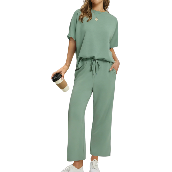 Woman in a graceful green set with loose top and drawstring pants, holding a coffee, studio context.