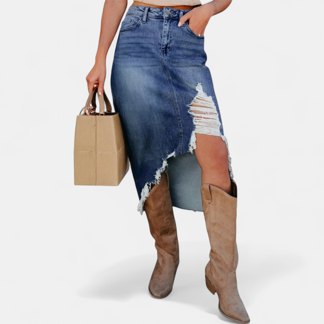Blue distressed high-waist denim maxi skirt with a beige handbag and tan boots in a studio setting.