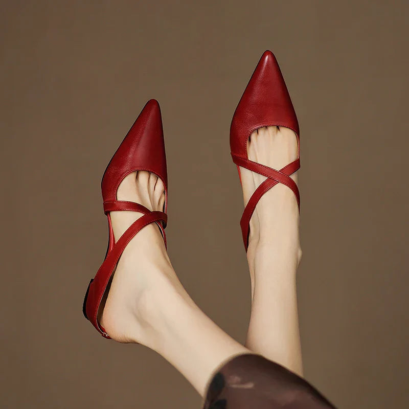 Red, black, and tan mules with criss-cross straps on a textured surface.