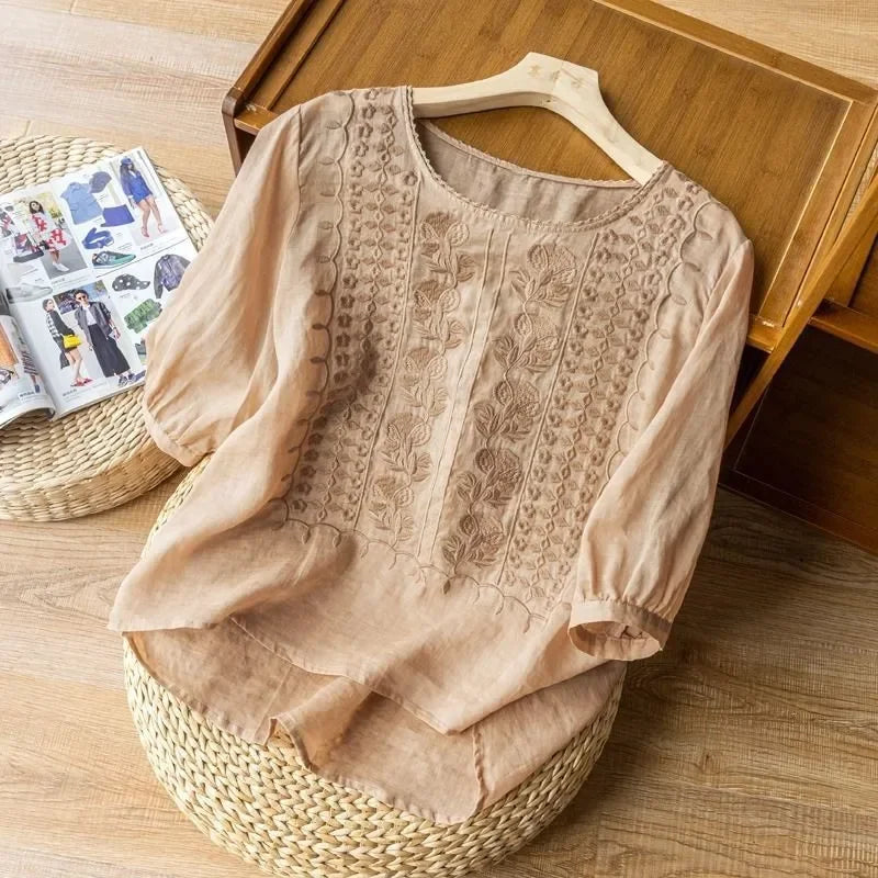 Peach elegant soft blouse with fine embroidery placed on wicker stool, wooden floor setting.