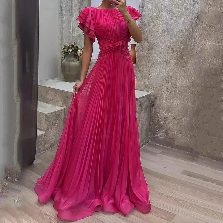 Vibrant pink pleated evening dress with ruffled sleeves, set in a sophisticated indoor environment with elegant accents.