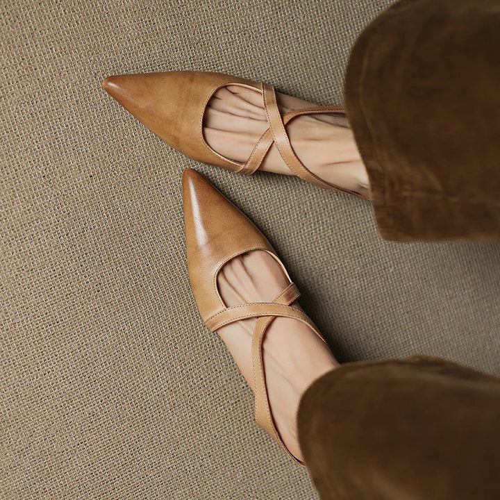 Top view of tan mules with criss-cross straps on a textured surface.