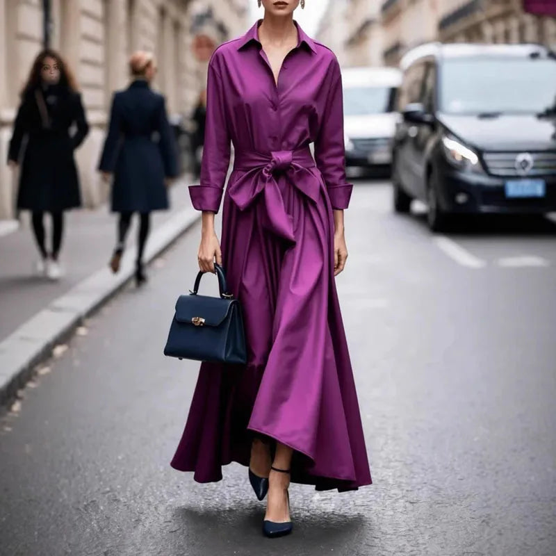 Rich purple maxi dress featuring a tied waist, matched with a dark handbag and shoes, walking on an urban street.