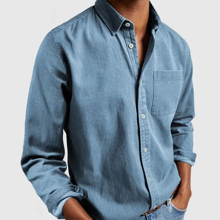 Light blue button-up shirt with front pocket and rolled sleeves, styled with hands in pockets against a gray backdrop.