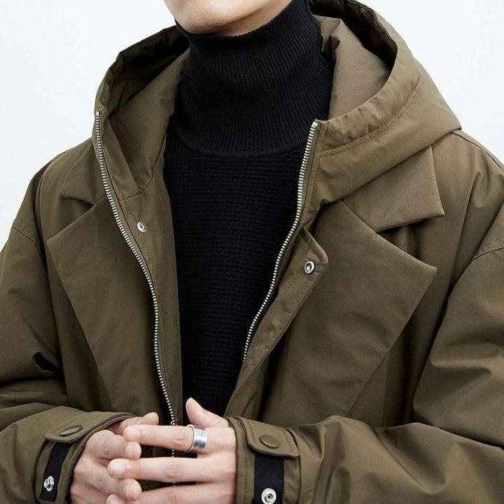 Close-up of a person in a brown long coat with a hood and turtleneck, in a studio.