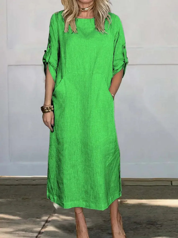 Green A-line loose fit draped evening dress, studio setting with wooden floor and pale wall background.