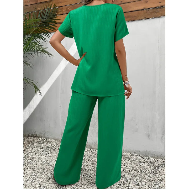 Back view of green soft, flowing two-piece set with short-sleeve top and wide-leg pants, outdoors near wooden fence.