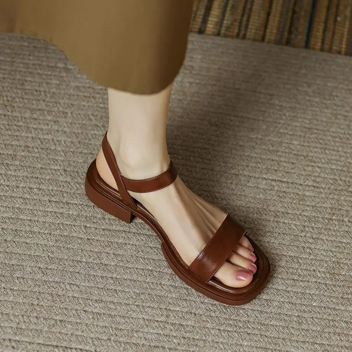Brown sandals on foot, textured surface, wearing brown dress.