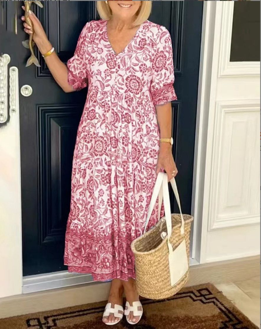 Woman in a red floral V-neck dress holding a straw bag, by a dark door.