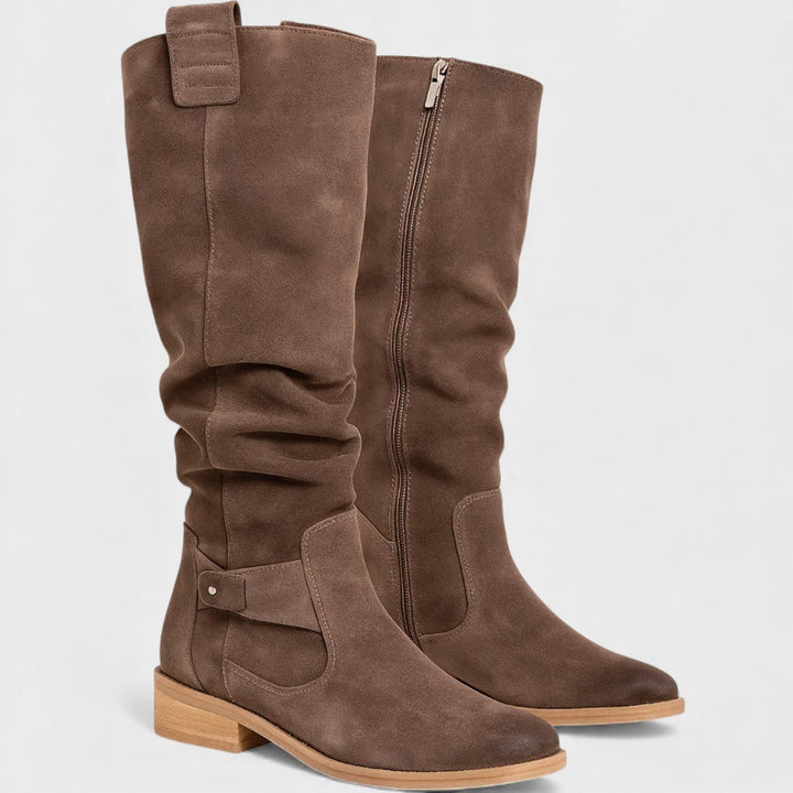 Pair of brown knee-high boots with buckle detail, zipper, and wooden heels, studio background.