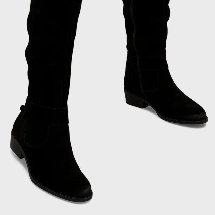 Close-up of black knee-high boots with buckle detail and heels, studio background.