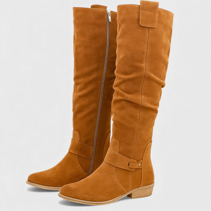 Pair of orange knee-high boots with buckle detail, zipper, and wooden heels, studio background.