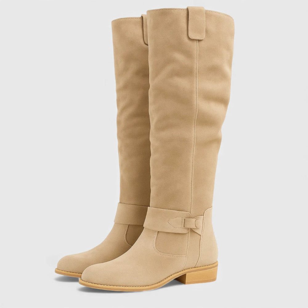 Pair of tan knee-high boots with buckle detail and wooden heels, studio background.