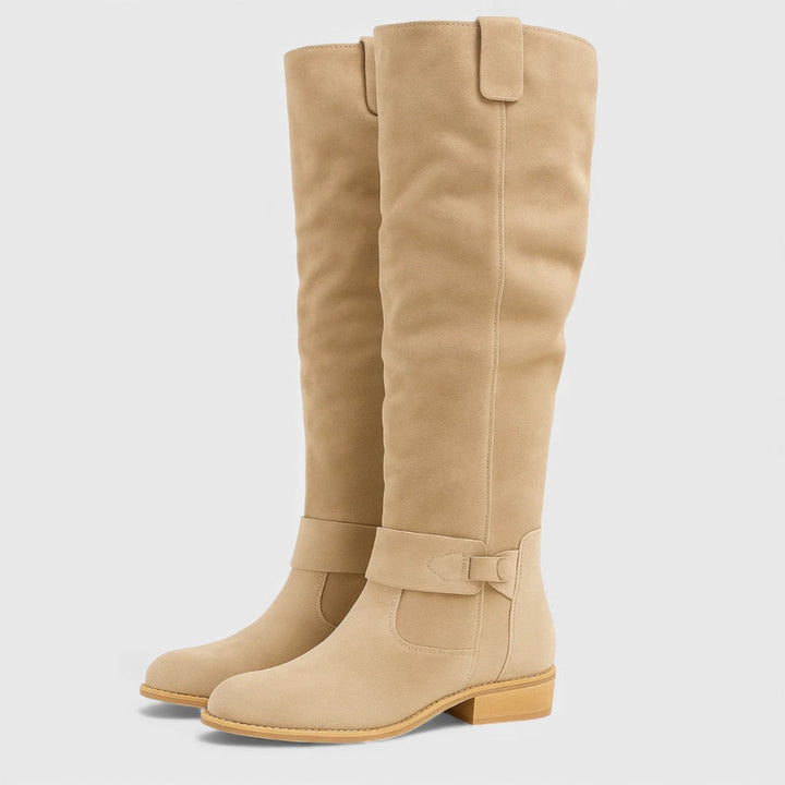 Pair of tan knee-high boots with buckle detail and wooden heels, studio background.