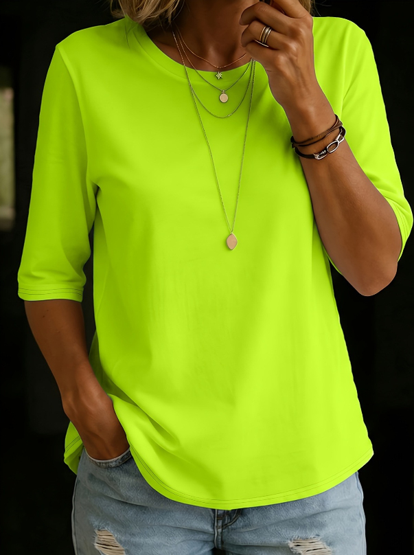 Bright green three-quarter sleeve tee with layered necklaces, worn with light blue distressed jeans, in a dark setting.