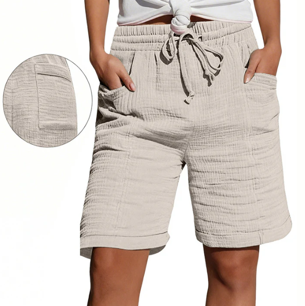 Beige Bermuda shorts with elastic waist, drawstring, pockets, and textured fabric. Modeled outdoors.