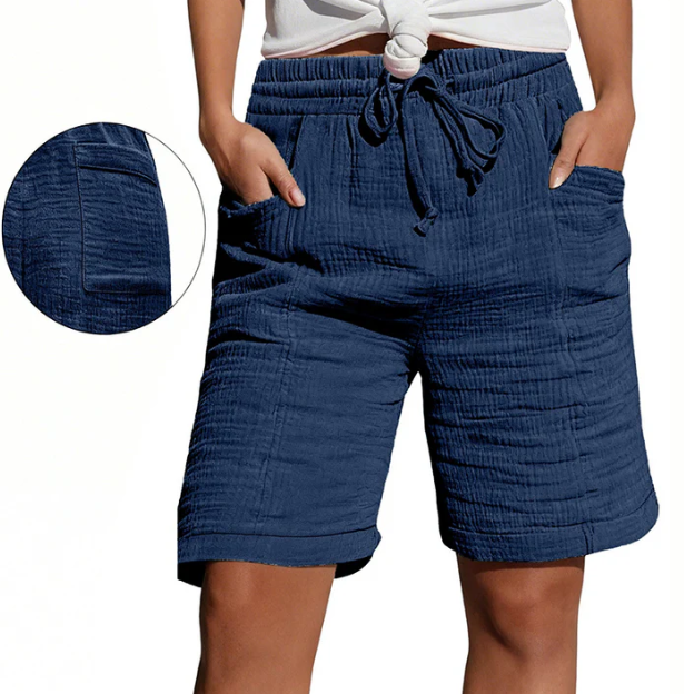 Dark blue Bermuda shorts with elastic waist, drawstring, pockets, and textured fabric. Modeled outdoors.