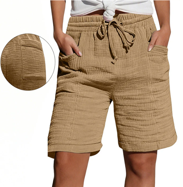 Tan Bermuda shorts with elastic waist, drawstring, pockets, and textured fabric. Modeled outdoors.