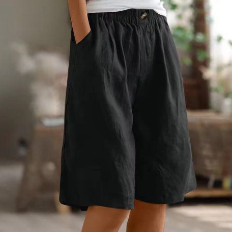 Black comfort shorts with stretchy waistband and pockets, displayed in a softly lit, homey indoor space.