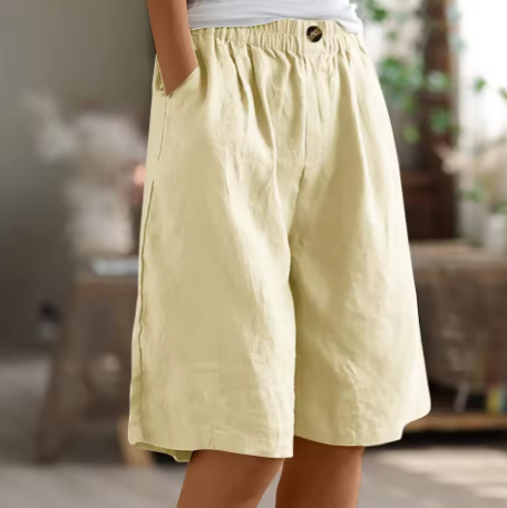 Beige comfort shorts with a stretchy waistband and pockets, displayed in a softly illuminated indoor setting.