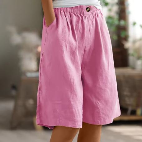 Pink comfort shorts featuring pockets and an elastic waistband set in a warmly lit indoor environment.