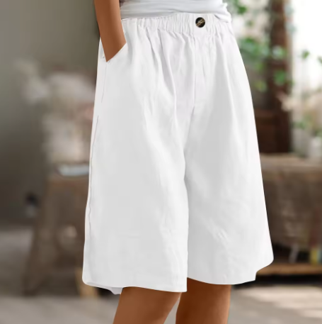 White comfort shorts with elastic waistband and pockets set in a warmly lit indoor environment.
