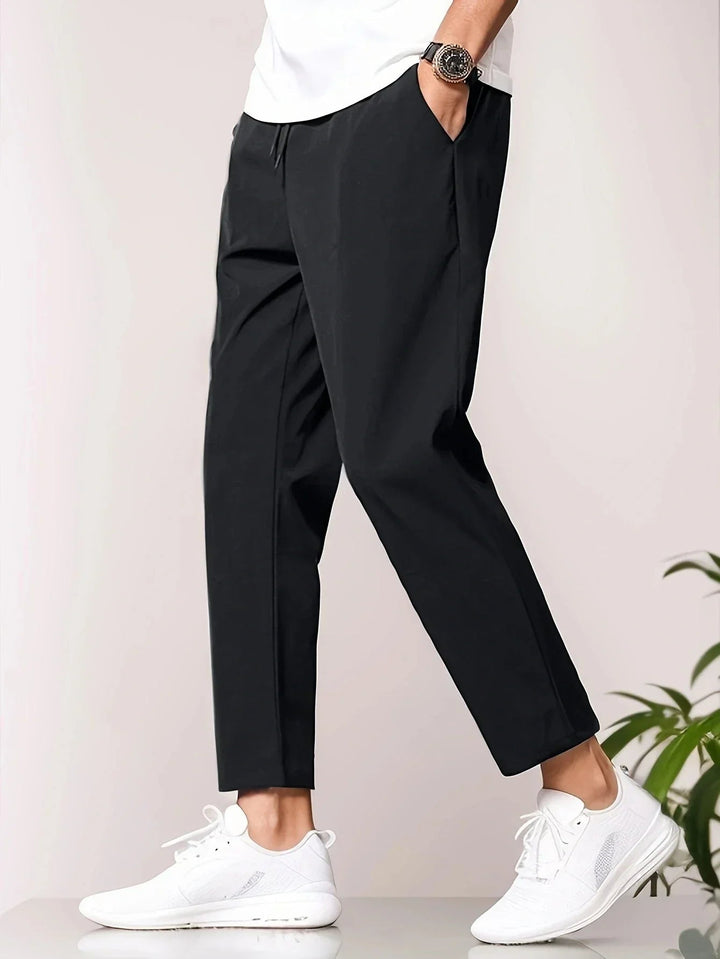 Casual black pants with a white top, complemented by white sneakers, studio background.