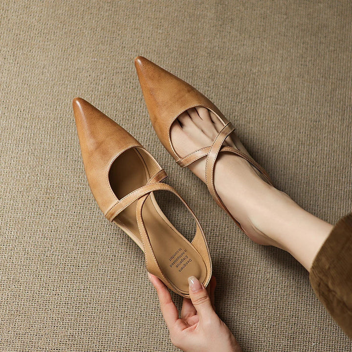 Tan pointed mules with criss-cross straps on a beige textured surface.